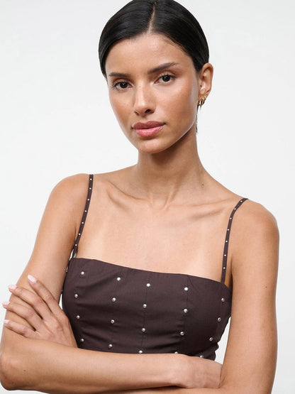 Woman with straight dark hair in a low bun wears the STAUD Wylie Dress in Earth Studs, a brown sleeveless dress with silver studs, standing with arms crossed against a plain background.