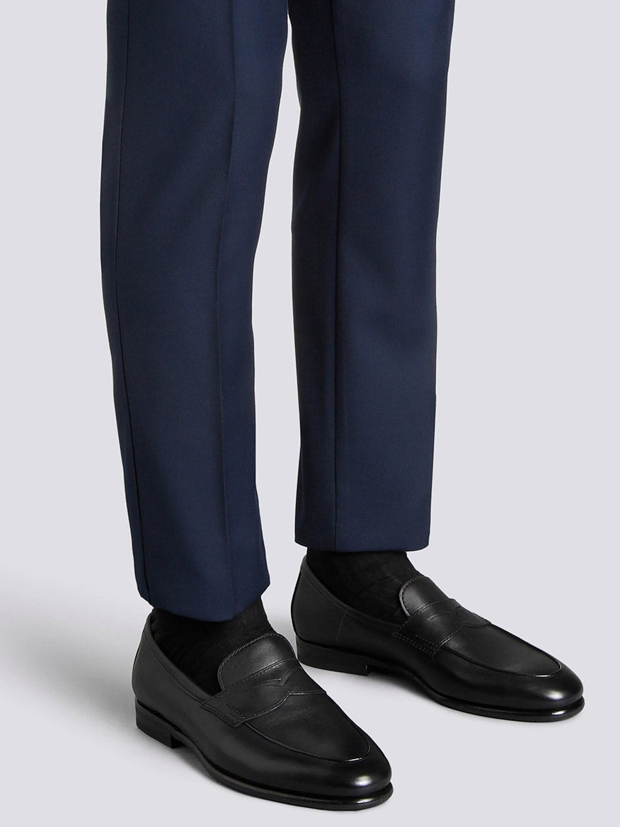A person wearing navy blue dress pants, black socks, and the Santoni Carlos Black Leather Penny Loafer stands against a plain light grey background.