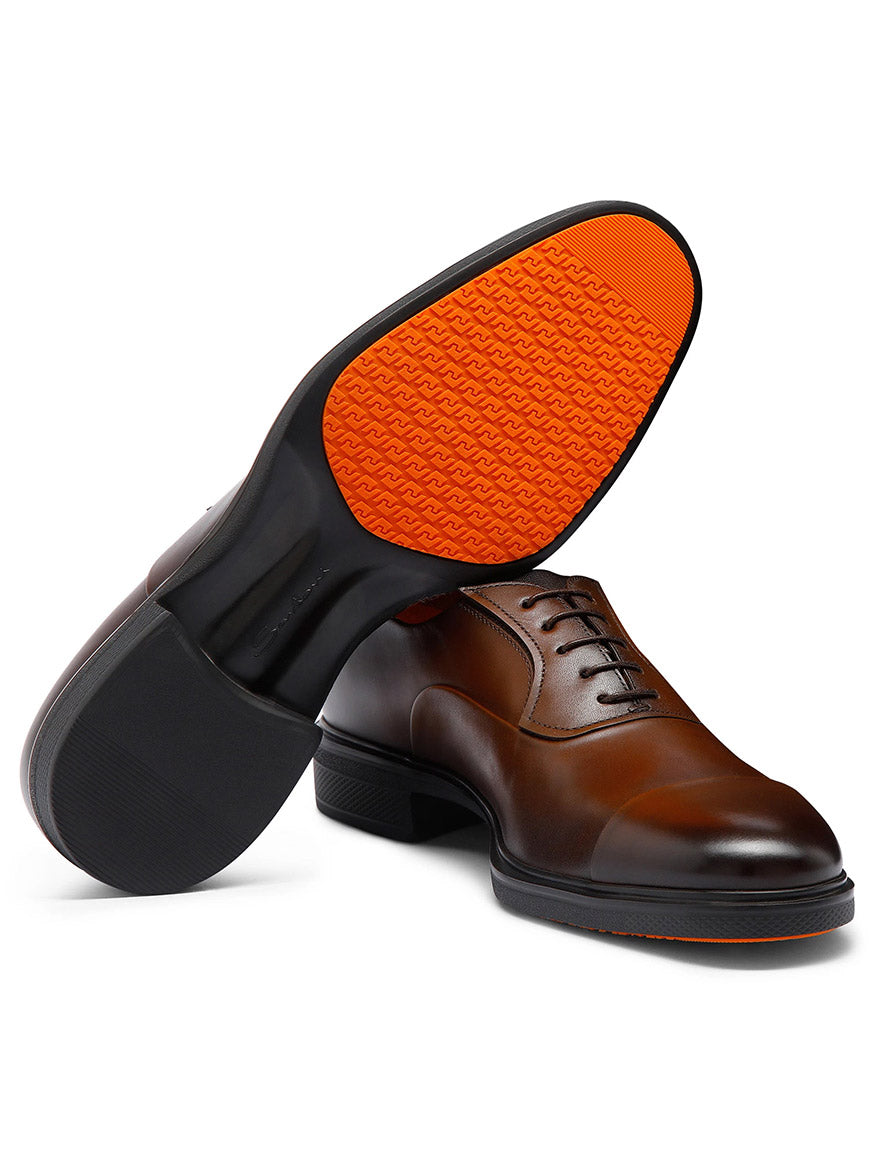 The Santoni Easy Lace-Up Oxford in Dark Brown features brown leather, black soles, and orange patterned rubber detailing underneath, highlighting Italian craftsmanship.