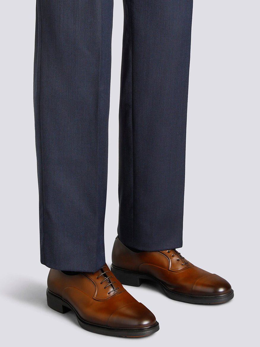 A person wearing dark navy dress pants and Santoni Easy Lace-Up Oxford shoes in dark brown, renowned for Italian craftsmanship, stands on a light gray background.