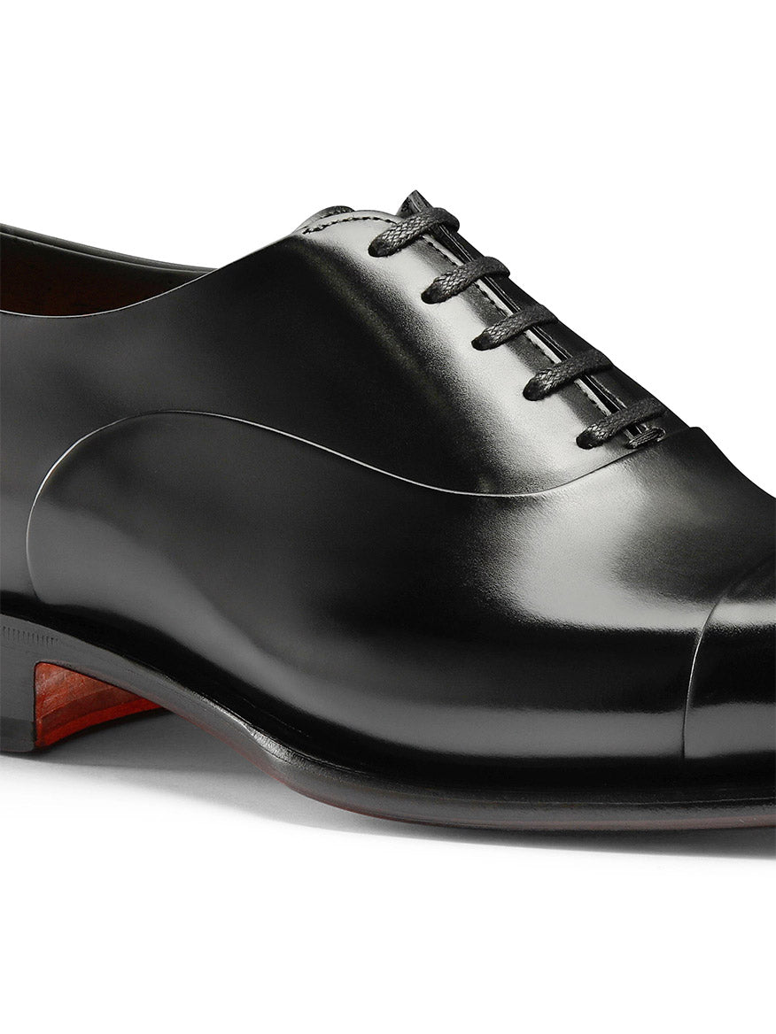 Presenting the Santoni Isaac Balmoral Oxford in Black: A sleek, polished leather shoe with black laces, low wooden heel, and Goodyear construction for durability and refined style.