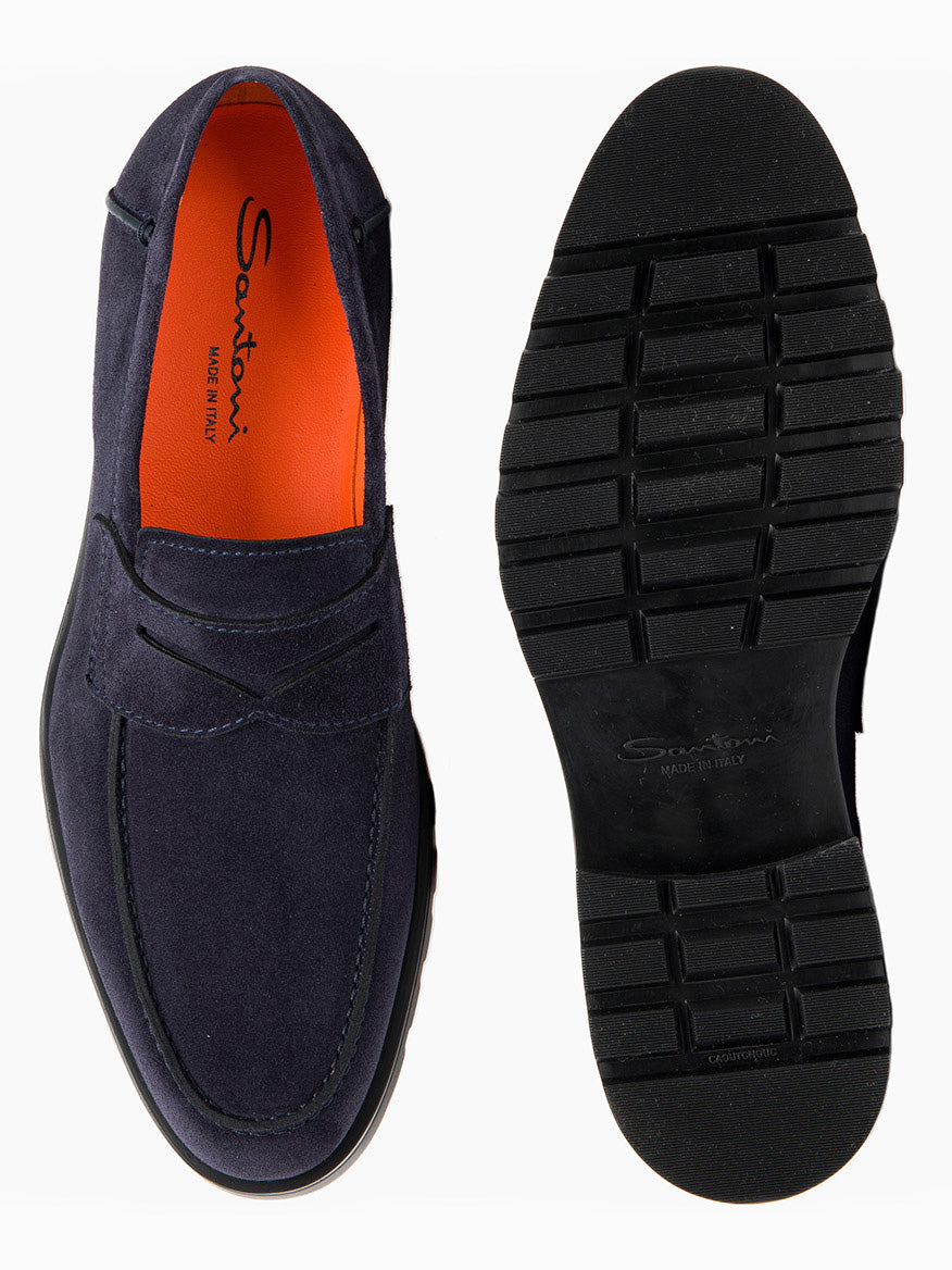 A pair of Santoni Rock Suede Lug Sole Penny Loafers in Navy with vibrant orange insoles is shown. One loafer, featuring a penny keeper strap, is positioned to display the top view, while the other showcases its sole, revealing an intricate tread pattern. This elegant slip-on style combines sophistication with effortless wearability.