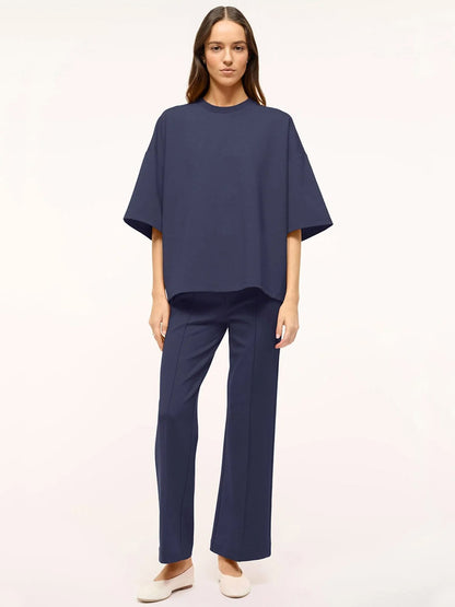 A person in a loose-fitting navy STAUD Capsule Top with wide sleeves, made of ponte fabric, stands against a plain background.