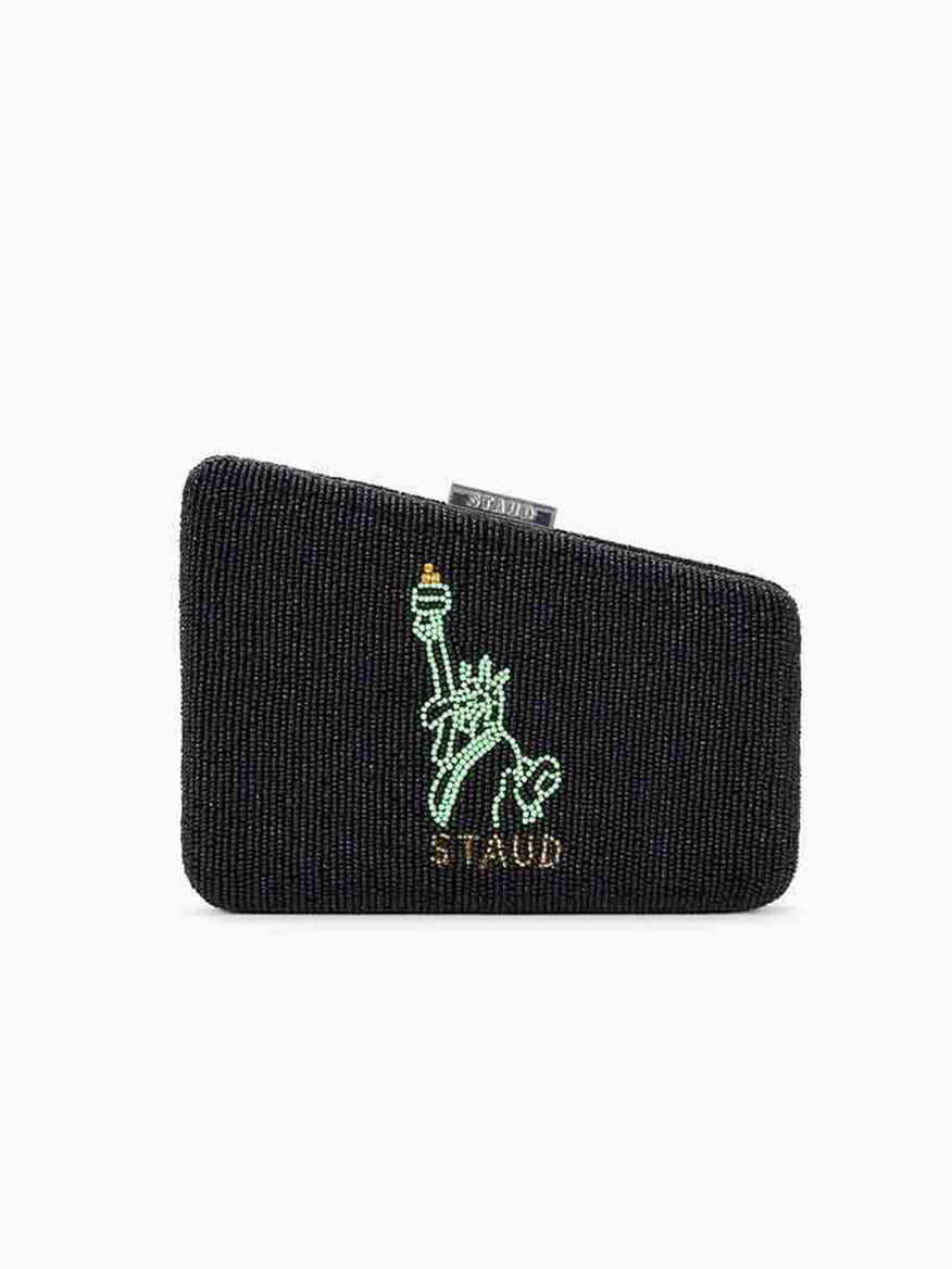 The STAUD Carmella Beaded Clutch NYC Skyline is a black evening clutch with a distinctive beaded texture, showcasing an embroidered green statue above the word "STAUD." It includes a removable chain strap and embodies the elegance of an NYC skyline design.