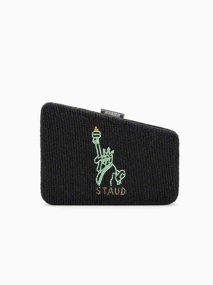 The STAUD Carmella Beaded Clutch NYC Skyline is a black evening clutch with a distinctive beaded texture, showcasing an embroidered green statue above the word "STAUD." It includes a removable chain strap and embodies the elegance of an NYC skyline design.