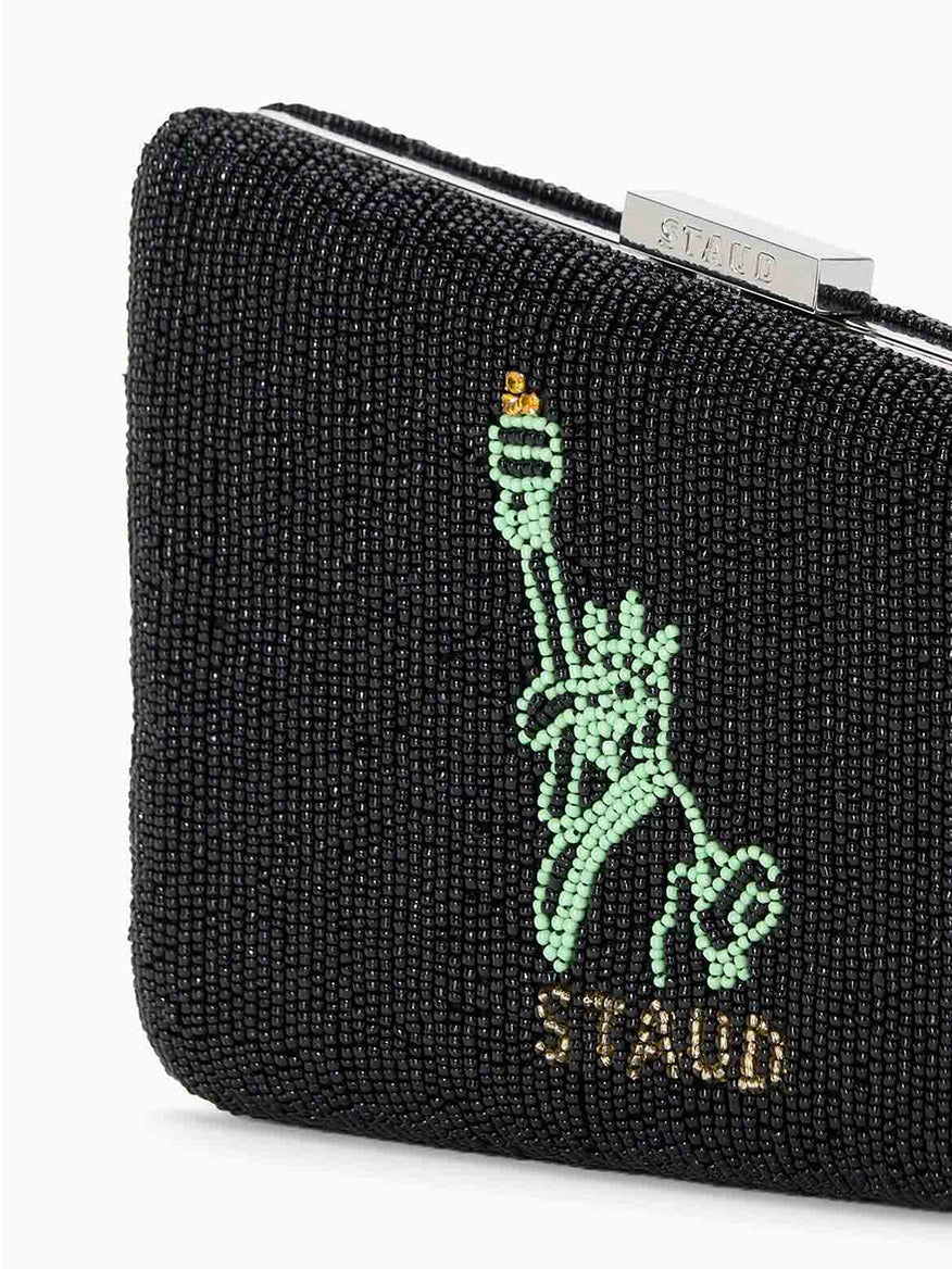 The STAUD Carmella Beaded Clutch NYC Skyline is a chic black beaded evening bag featuring a green beaded Statue of Liberty design and the word "STAUD" at the bottom, complete with a removable chain strap for versatile wear.