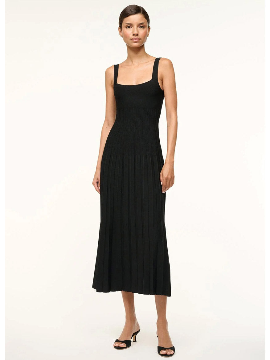 A person wearing the STAUD Ellison Sleeveless Dress in Black, which features a square neck and ottoman stitch detailing, stands against a plain white backdrop.