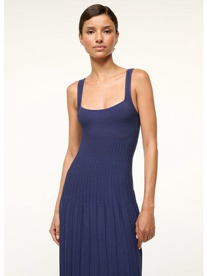 Standing against a plain background, a person wears the STAUD Ellison Sleeveless Dress in navy, featuring ottoman stitch detailing and a square neckline.