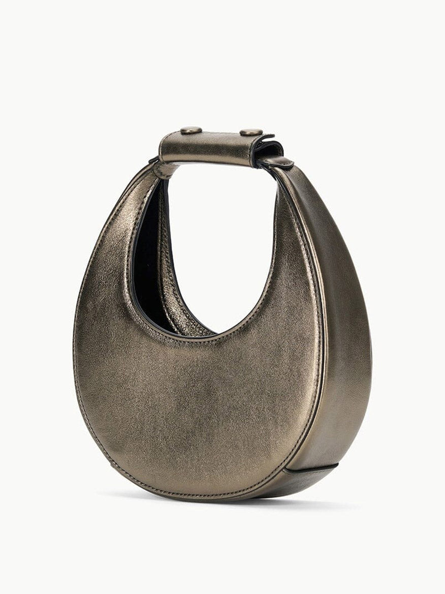 The STAUD Goodnight Moon Bag in Aged Bronze is a metallic bronze leather evening bag with a unique circular shape and a broad leather shoulder strap extending across the top.