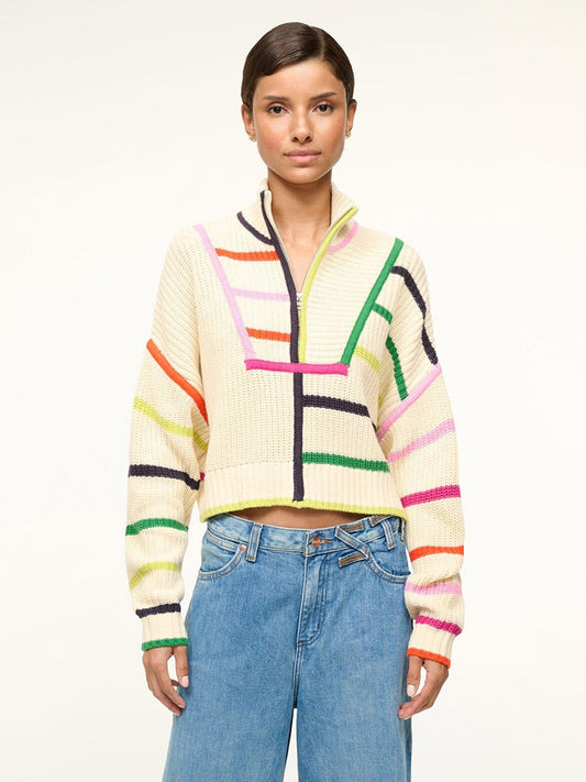 A person in a STAUD Cropped Hampton Sweater in Cream/Rainbow Multi with blue jeans stands against a plain background.