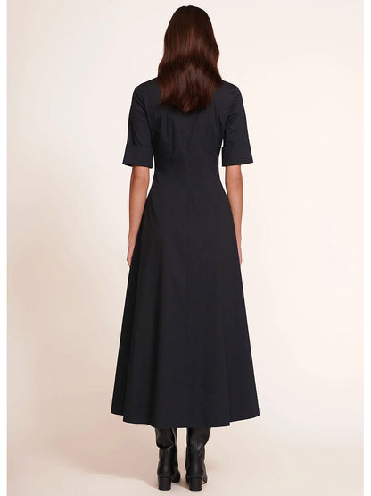 Back view of a person with long hair wearing the chic STAUD Joan Maxi Dress in Black, a half-sleeve, ankle-length shirt dress crafted from stretchy cotton poplin, seamlessly paired with stylish black boots.