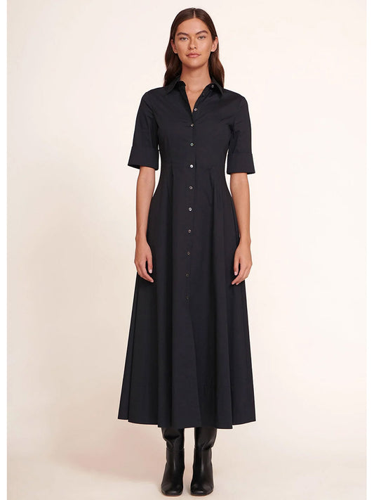 A person stylishly wears the STAUD Joan Maxi Dress in Black, a maxi shirt dress made of stretchy cotton poplin, paired with black boots against a plain background.