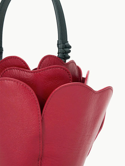 The STAUD Juliet Bag in Rouge, featuring a petal-shaped design with a black handle, is shown against a plain background, capturing the allure of a true novelty accessory.