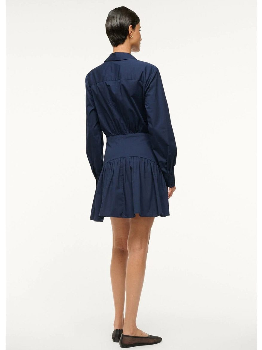 A person wearing the stylish STAUD Rocco Mini Dress in navy long sleeves with black flats stands facing away.