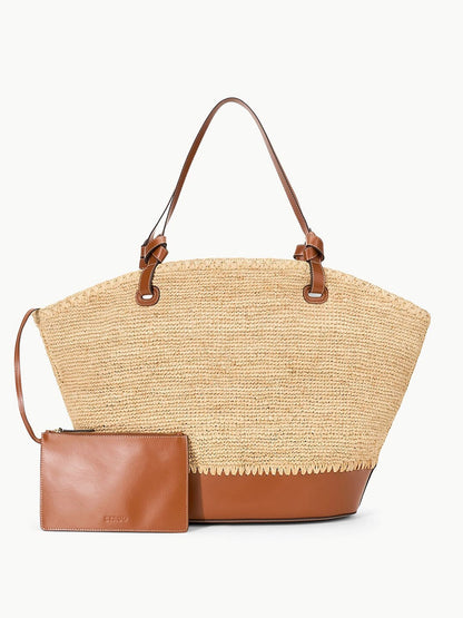 The STAUD Squillo Raffia Tote in Natural/Tan is an oversized straw tote bag featuring brown leather handles and trim, and it comes with a matching brown leather pouch.