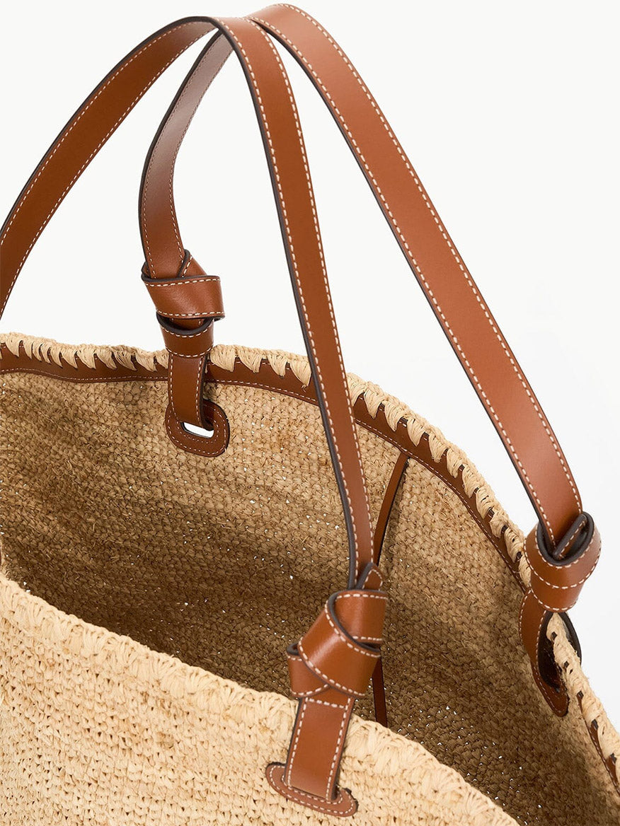 Close-up of the STAUD Squillo Raffia Tote in Natural/Tan, showcasing leather handles and intricate stitching details.