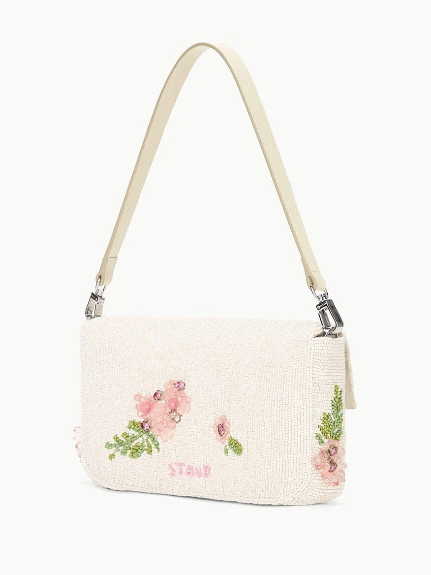 The STAUD Timmy Shoulder Bag in Magnolia is a white beaded vegan leather shoulder bag, featuring a removable beige strap, floral embroidery and beadwork in pink and green tones, and finished with a convenient magnetic closure.