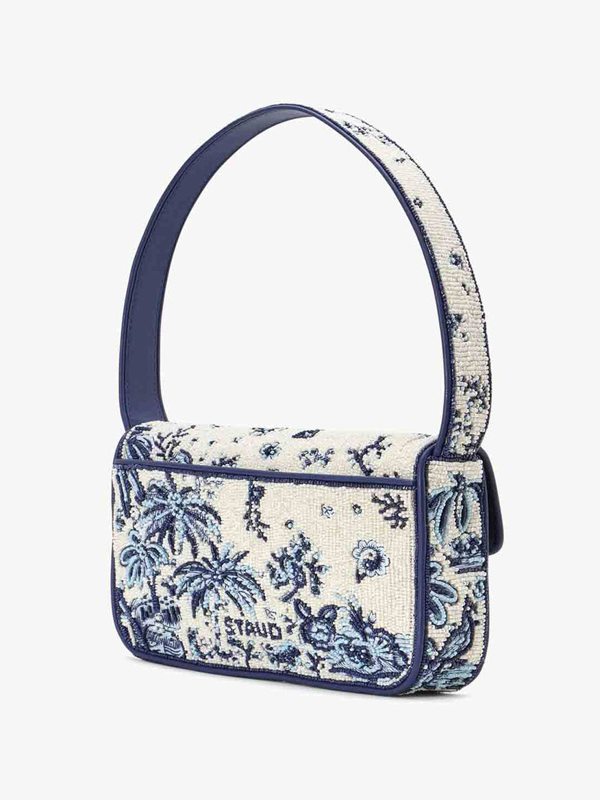 Introducing the STAUD Tommy Beaded Bag in Toile de Pup, a rectangular handbag designed with a tropical blue and white floral pattern, complete with a wide strap and made from vegan leather for an eco-friendly flair.