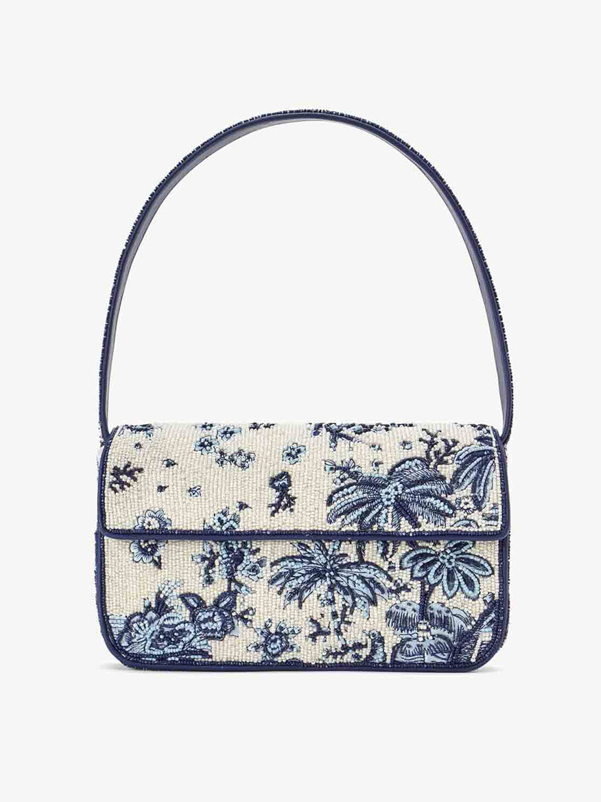 The STAUD Tommy Beaded Bag in Toile de Pup is a distinctive handbag adorned with an embroidered floral and bird pattern in hues of blue and white, crafted from vegan leather, and featuring a single strap with a flap closure.