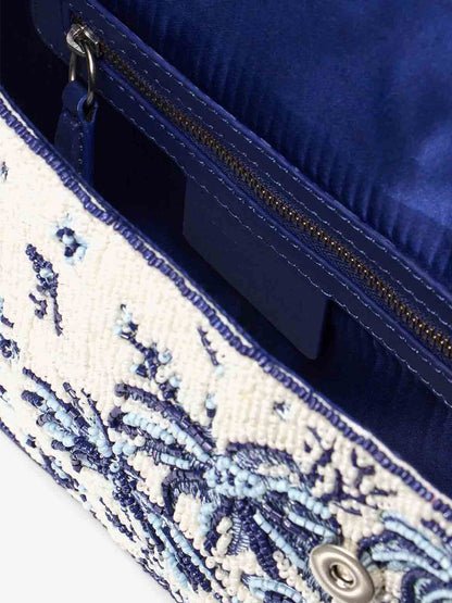 Close-up of the STAUD Tommy Beaded Bag in Toile de Pup, highlighting its embellished clutch purse design with a distinctive blue and white pattern. The interior is lined with blue fabric and includes a zippered pocket, seamlessly blending style and practicality.