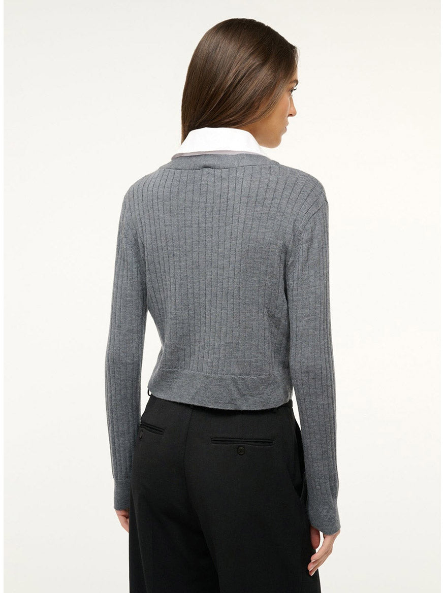 Person with long brown hair standing with their back to the camera, wearing a STAUD Wallis Sweater in Charcoal/White over a removable cotton poplin collared bib and black pants.