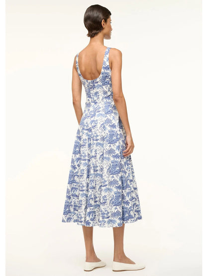 A woman models the STAUD Wells Sleeveless Dress in Blue Toile, crafted from cotton poplin with a scoop back. She stands sideways, highlighting its fitted shape, and pairs it with white flats.