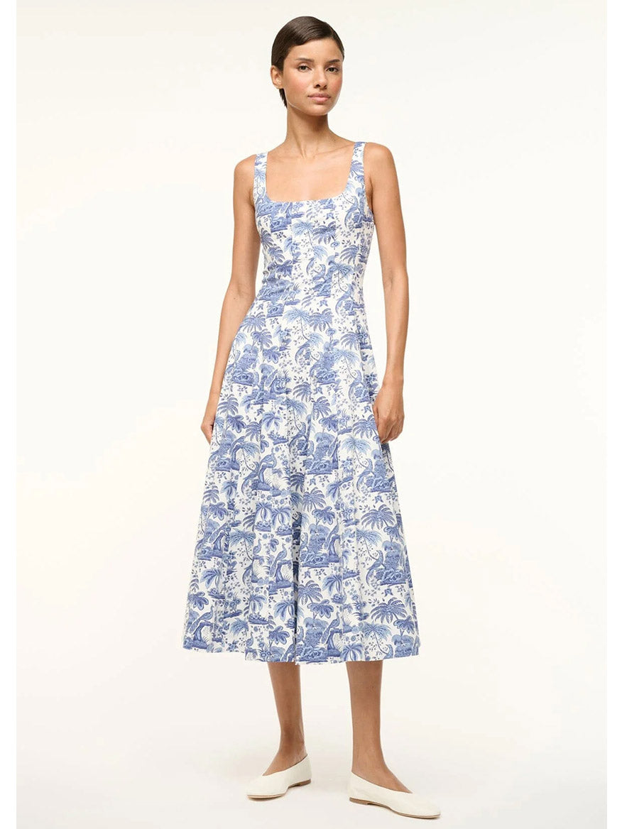 A person models the STAUD Wells Sleeveless Dress in Blue Toile, featuring a fitted shape and blue and white pattern, paired with white shoes against a plain background.