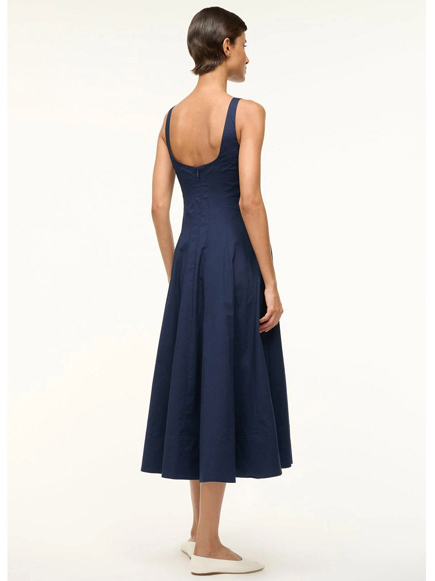 Dressed in the STAUD Wells Sleeveless Dress in Navy and white flats, a person stands against a plain background.