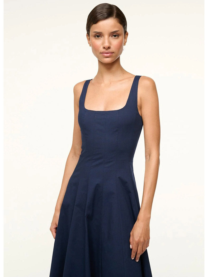 A woman in the STAUD Wells Sleeveless Dress in Navy stands against a plain background, her hair pulled back and wearing a neutral expression.