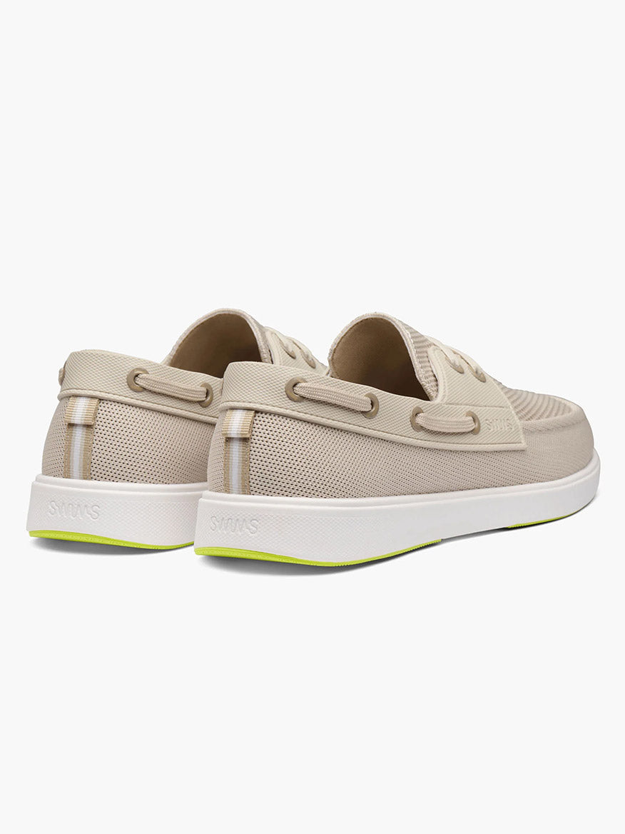 The Swims Breeze Boat Shoe in Mist/Sand is a beige slip-on with white soles and light green bottom accents, designed for lightweight comfort, shown from the back.