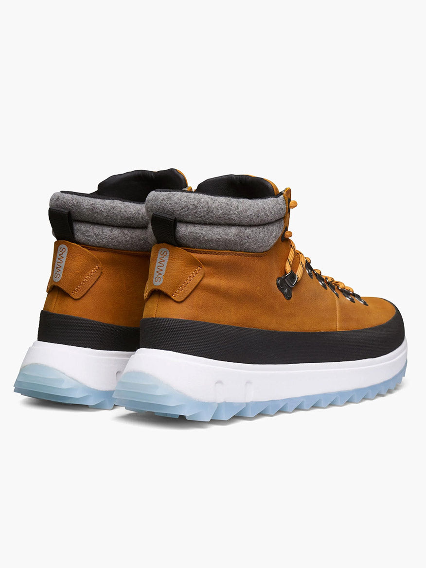 The Swims Fjell Boot in Blaze is a pair of brown waterproof leather hiking boots with thick white and blue soles, gray padded ankle collars, and lace-up fronts, shown from the back.