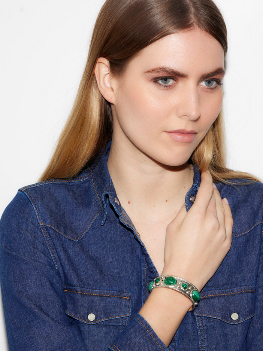 A person with long hair wears a denim shirt and holds their hand near their face, showcasing the Sylvia Toledano Cuff Byzantine in Malachite & Silver.