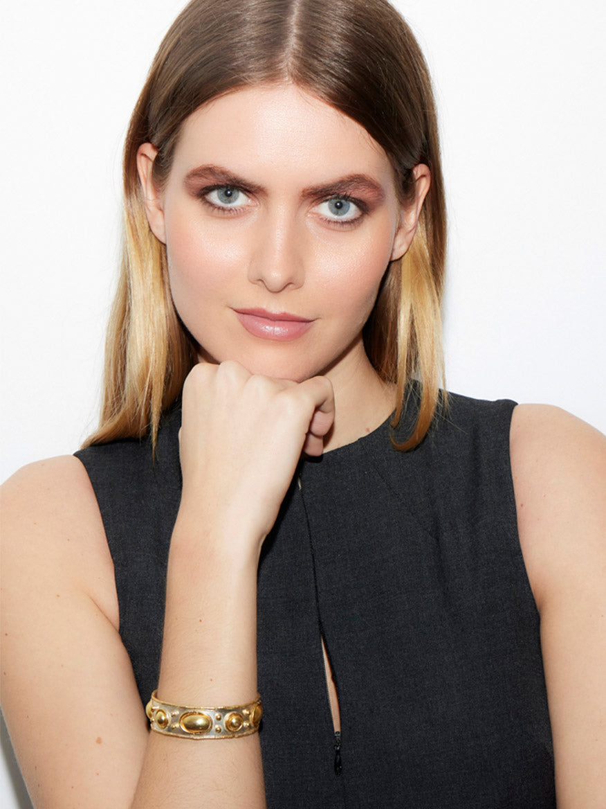 A person with long hair, wearing a sleeveless dark top and the eye-catching Sylvia Toledano Cuff Byzantine in Gold and Silver, rests their chin on their hand while gazing at the camera.