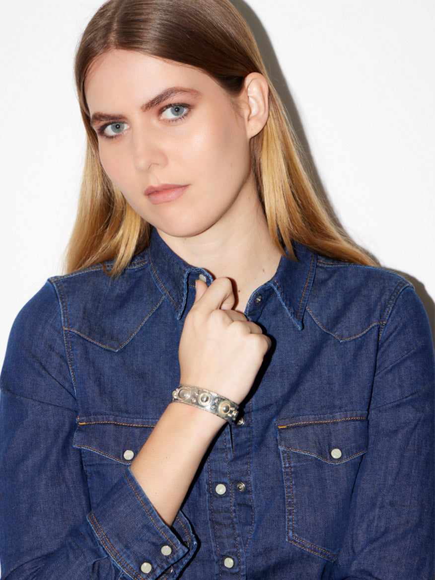 A person with long hair, wearing a denim shirt and a Sylvia Toledano Cuff Byzantine in Silver, looking straight at the camera.