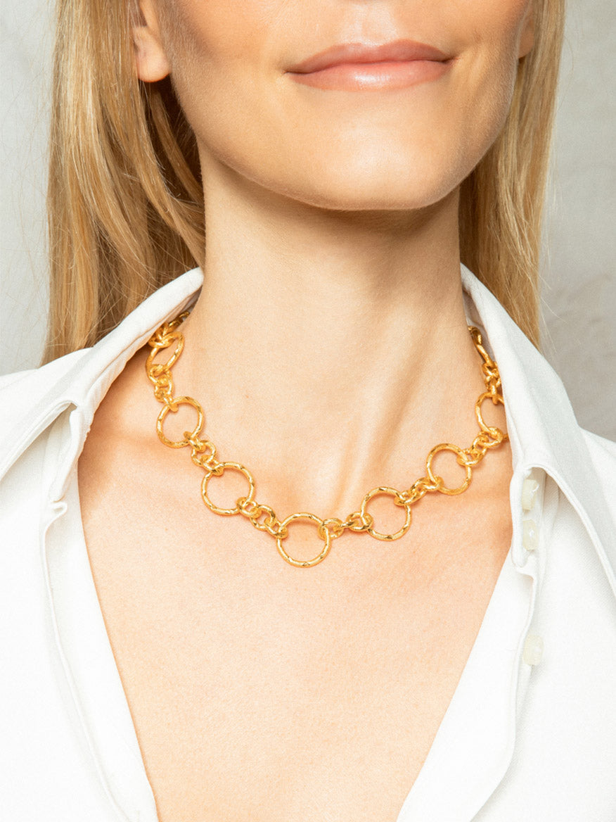 A person wears a Sylvia Toledano Pendant Saturn Chain in Gold, its dazzling loop design perfectly complementing the crisp white collared shirt.