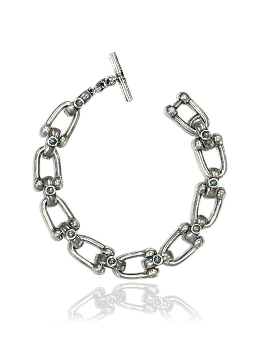 The Tat2 Designs Brioni Horseshoe Bracelet in Vintage Silver features blue gemstones and a custom toggle closure, displayed on a white background.