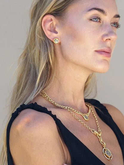 A woman with long blonde hair wears the Tat2 Designs Miko Coin Necklace in Gold & Vintage Silver, gold earrings, and a black sleeveless top, looking to the side in natural light.