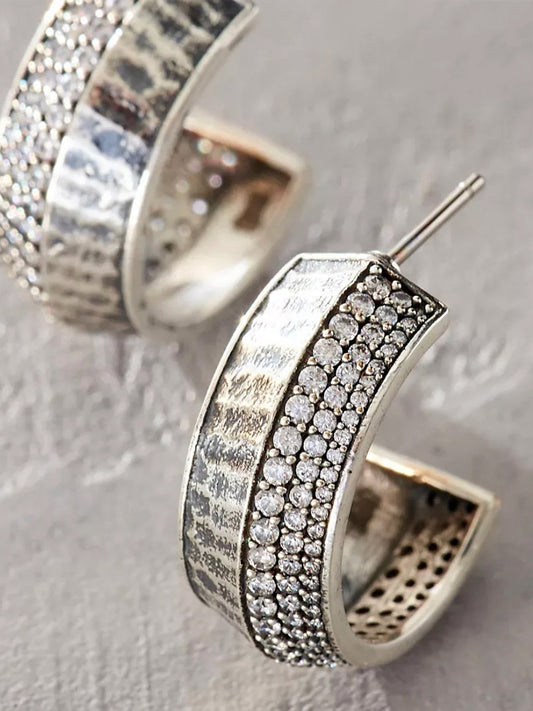 Close-up of Tat2 Designs Pave Noma Hoops in Vintage Silver, showcasing sterling silver hoops with a textured surface and a row of clear round cubic zirconia along the outer edge.