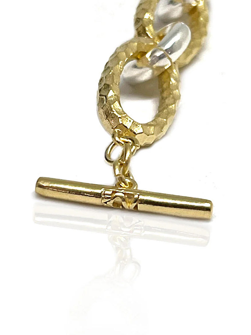 Close-up of the Tat2 Designs Ravelle Hammered Chain Bracelet in Gold Two-Tone, showcasing custom metal textures and a toggle clasp with gold and clear links, photographed on a white background.