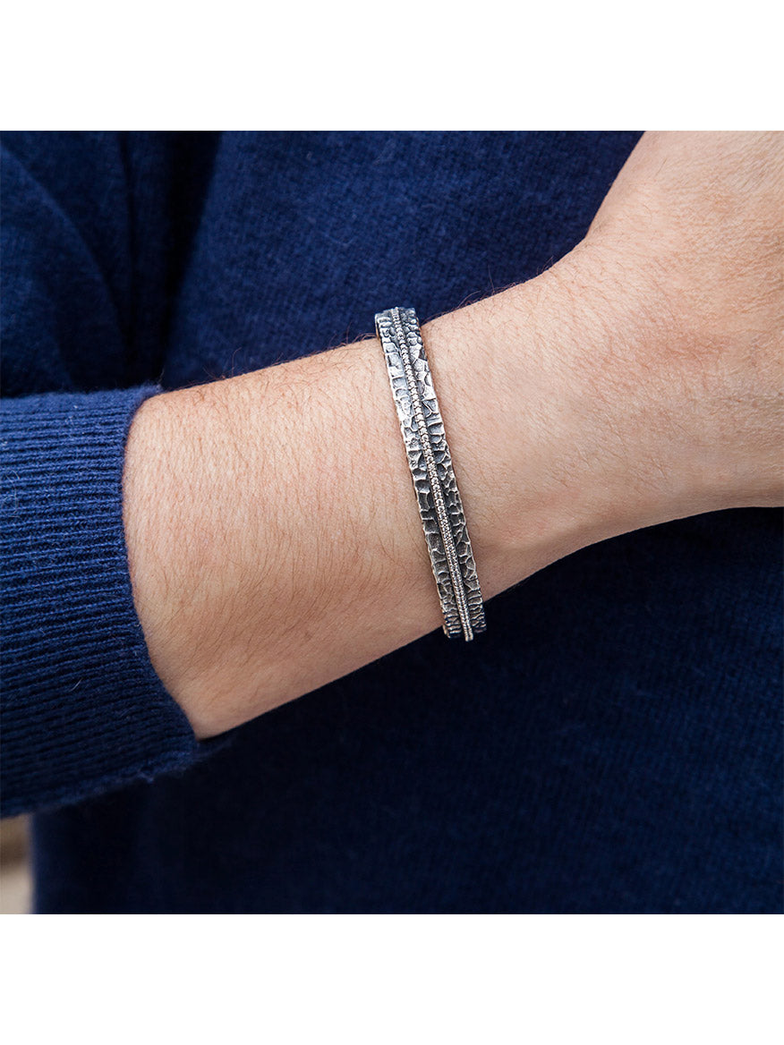 A person wearing the Tat2 Designs Egy Crystal Line Bangle in Vintage Silver on their wrist over a dark blue long-sleeve shirt.