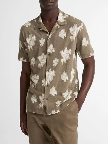 A man wearing the Vince Blurred Roses Short-Sleeve Button-Front Shirt in Kalamata Combo, featuring a beige floral pattern, paired with tan pants, stands against a plain white background.