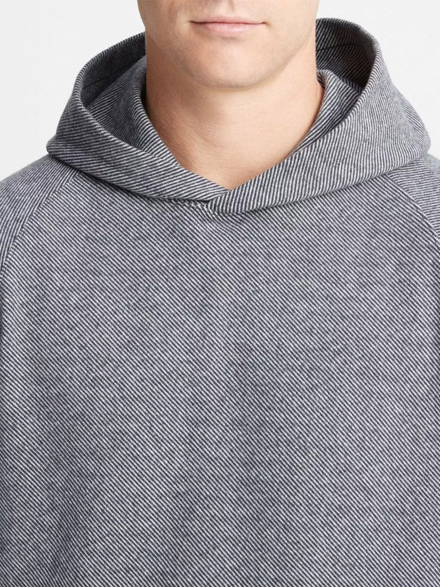 A person is dressed in a Vince Broken Twill Pullover Hoodie in Heather Grey/Off-White. The image focuses on the upper body and partial face, subtly emphasizing the remarkable comfort of the broken twill blend fabric.