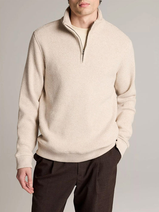 A man wears the Vince Brushed Cotton-Blend Waffle Quarter-Zip Pullover in Heather Oatmeal with dark pants, standing with one hand in his pocket against a plain background.