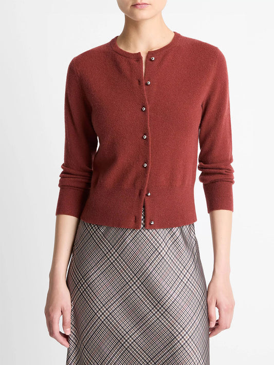 A woman wears the Vince Metal-Button Wool & Cashmere-Blend Cardigan in Siena, paired with a high-waisted plaid skirt, standing against a plain white background.