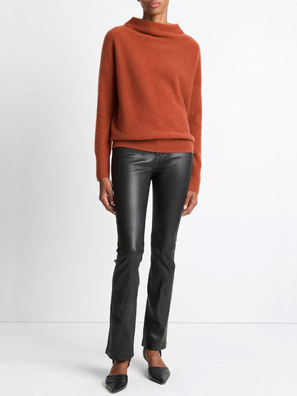 A person wearing the Vince Plush Cashmere Funnel-Neck Sweater in Tuscan Red, black faux leather pants, and black pointed shoes stands against a plain white background.