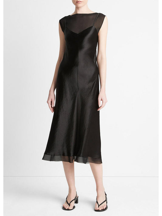 A person wearing a sleek black Vince Chiffon-Layered Satin Slip Dress in Black, made of Japanese Naia™ acetate satin with a sheer neckline, standing in black sandals. The dress has a mid-length hem and is modeled in a plain.