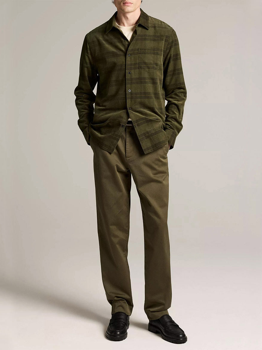 A person stands hands in pockets, wearing the Vince Hamilton Plaid Cotton Corduroy Button-Front Shirt in Night Leaf Combo, olive trousers, black shoes, and a white undershirt.