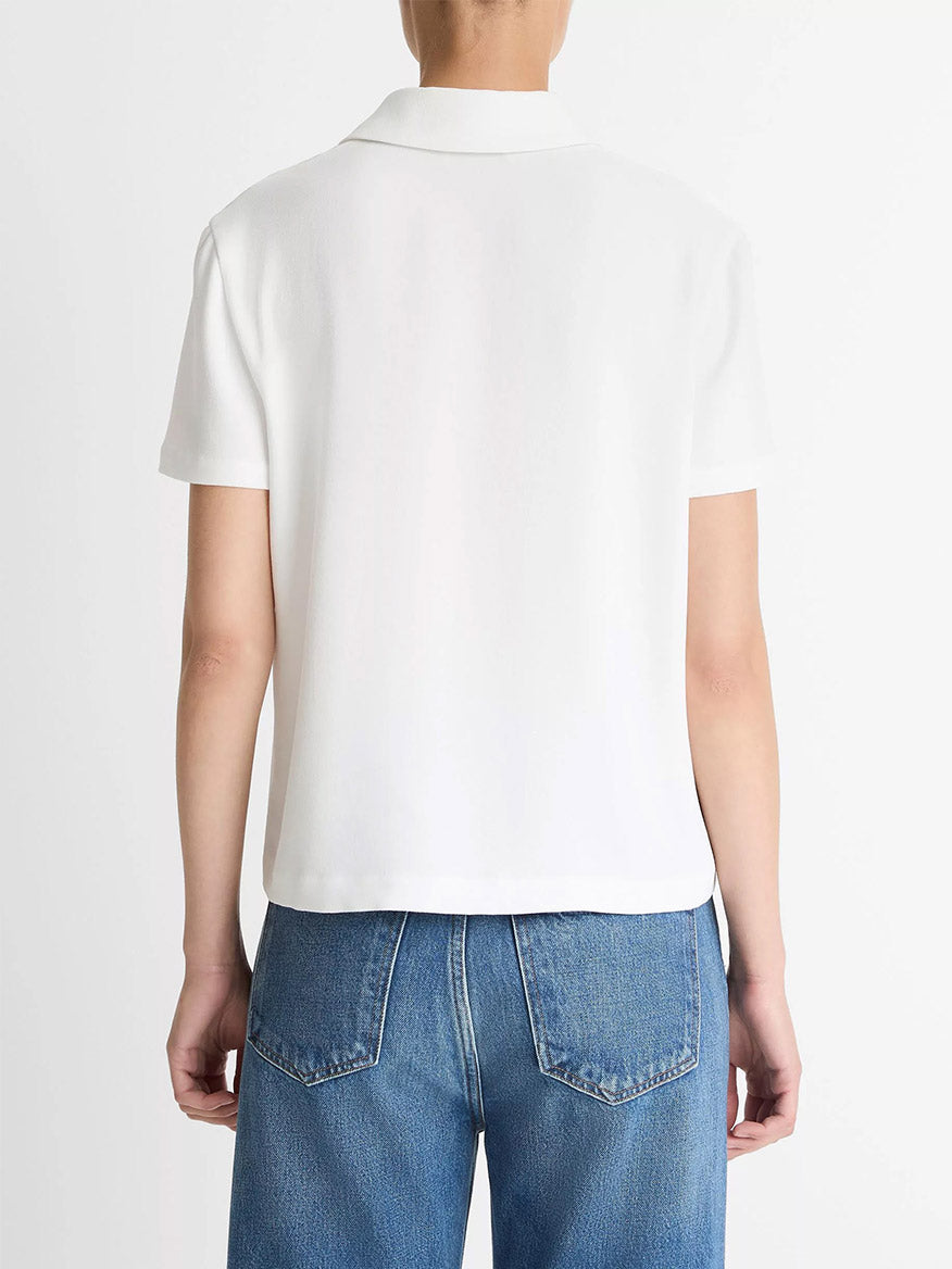 A person is shown from the back against a plain background, wearing blue jeans and the Vince Crepe Polo Shirt in off-white, featuring short sleeves and agoya shell buttons.