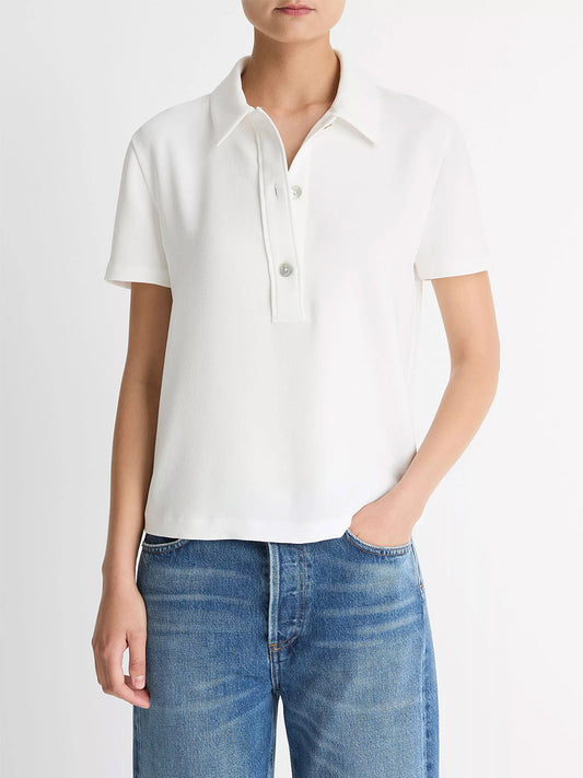 A person wears the Vince Crepe Polo Shirt in Off-White with blue jeans, featuring agoya shell buttons, standing against a plain white background.