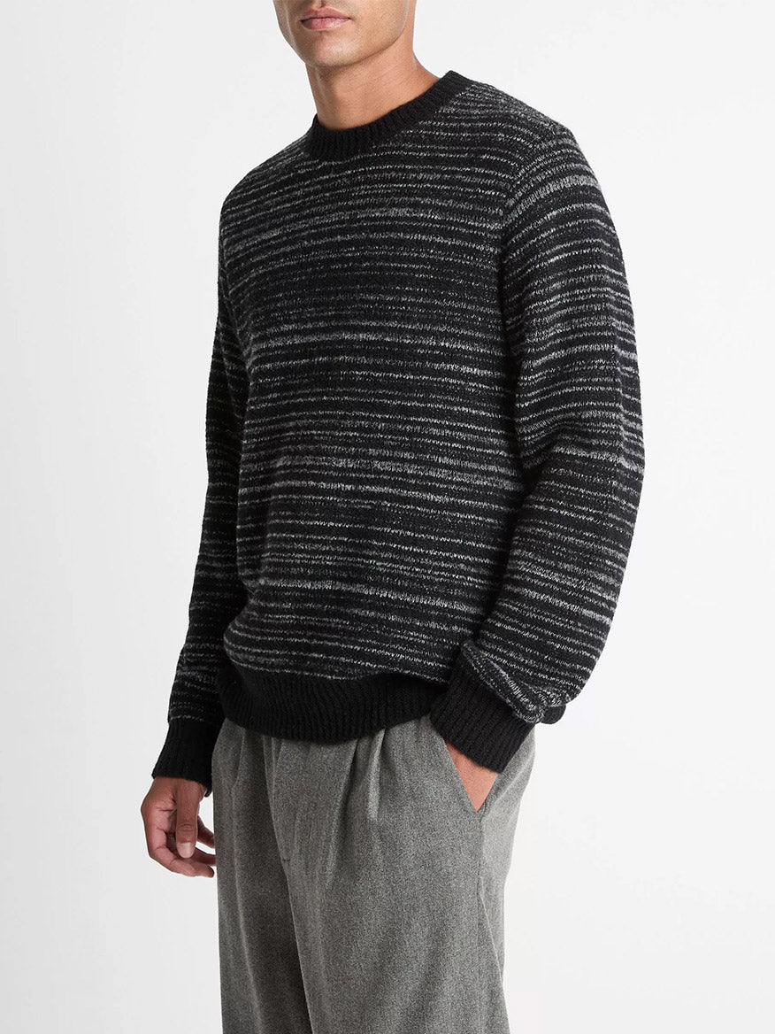 A man wearing the Vince Marled Stripe Merino Wool-Blend Sweater in Black with long sleeves and gray pants stands against a plain white background.